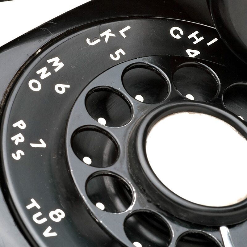 An old black vintage rotary style telephone off the hook isolated over a white background.