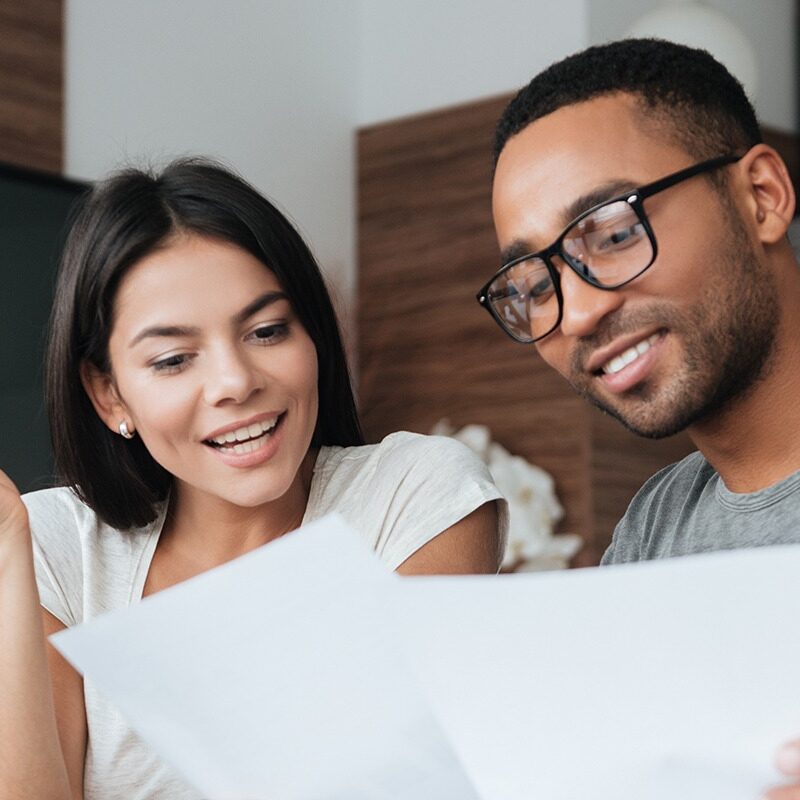 Cheerful loving young couple using laptop and analyzing finances Photo of cheerful loving young couple using laptop and analyzing their finances with documents. Look at papers.
